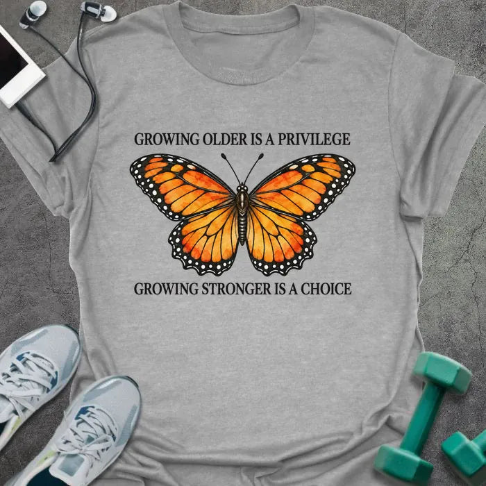 Sport grey t-shirt printed with "GROWING OLDER IS A PRIVILEGE, GROWING STRONGER IS A CHOICE" in black, with an orange watercolor monarch butterfly
