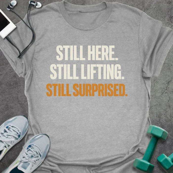 Sport grey t-shirt printed with "Still Here. Still Lifting. Still Surprised." in white and orange