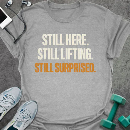 Sport grey t-shirt printed with "Still Here. Still Lifting. Still Surprised." in white and orange