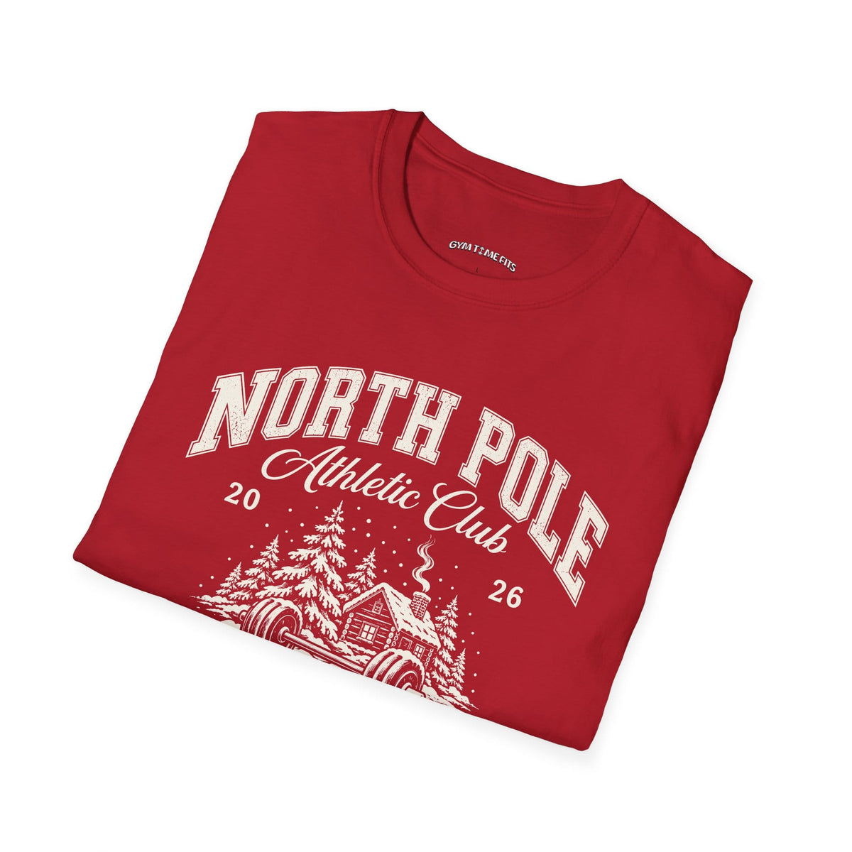 Folded cherry red t-shirt printed with "NORTH POLE Athletic Club 2026, Santa's Training Camp, MEMBERS ONLY" in cream, with snowy pine trees, a log cabin and a barbell in the snow
