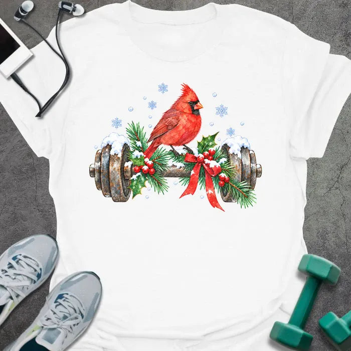 White t-shirt printed with a watercolor red cardinal perched on a snowy dumbbell trimmed with holly, pine branches and a red bow, with blue snowflakes