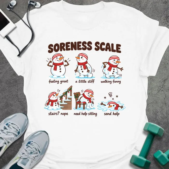 White t-shirt printed with "SORENESS SCALE" in brown, with six snowmen in striped headbands and red scarves labeled feeling great, a little stiff, walking funny, stairs? nope, need help sitting, and send help