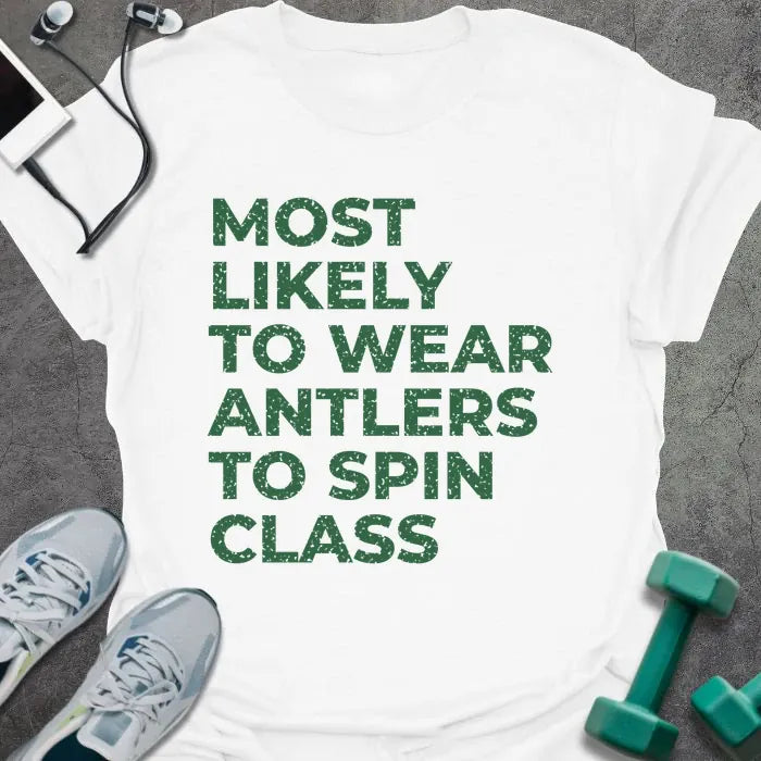White t-shirt printed with "MOST LIKELY TO WEAR ANTLERS TO SPIN CLASS" in green