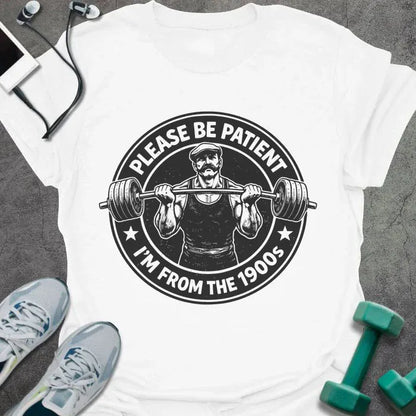 White t-shirt printed with "Please Be Patient I'm From the 1900s" in black, with a barbells and a retro strongman illustration