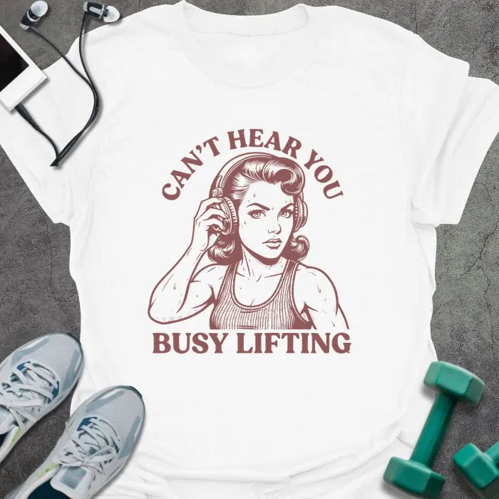 White t-shirt printed with "Can't Hear You Busy Lifting" in rust, with an illustration of a woman with headphones