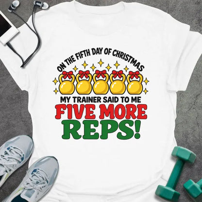 White t-shirt printed with "ON THE FIFTH DAY OF CHRISTMAS MY TRAINER SAID TO ME, FIVE MORE REPS!" in black, red and green, with five gold kettlebells tied with red bows