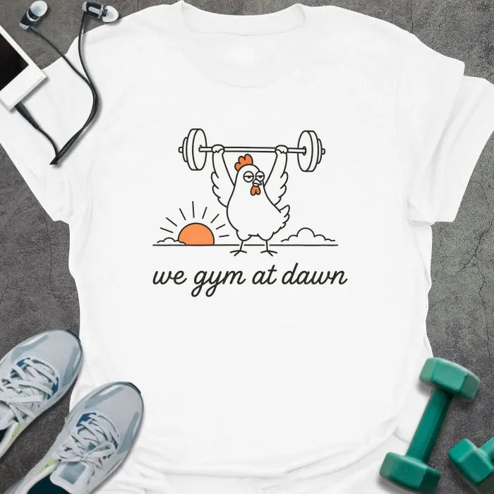 White t-shirt printed with "we gym at dawn" in orange, with a bird lifting weights at sunrise