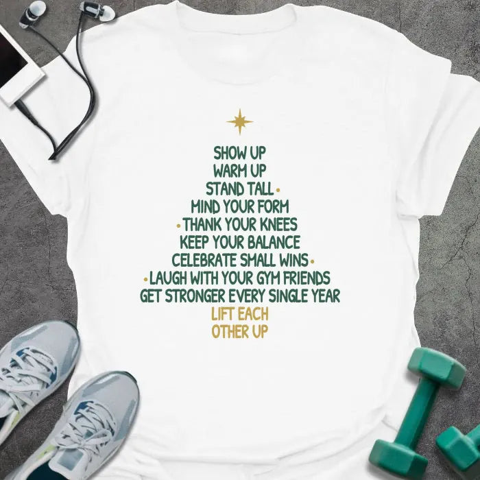 White t-shirt printed with a Christmas tree made of words, "SHOW UP, WARM UP, STAND TALL, MIND YOUR FORM, THANK YOUR KNEES, KEEP YOUR BALANCE, CELEBRATE SMALL WINS, LAUGH WITH YOUR GYM FRIENDS, GET STRONGER EVERY SINGLE YEAR, LIFT EACH OTHER UP", in green and gold with a gold star on top
