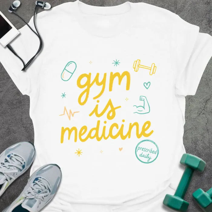 White t-shirt printed with "gym is medicine" in yellow, cyan, and orange, with dumbbell, heartbeat, and smiley graphics