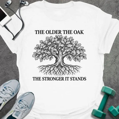 White t-shirt printed with "THE OLDER THE OAK, THE STRONGER IT STANDS" in black, with a drawing of an oak tree and its roots