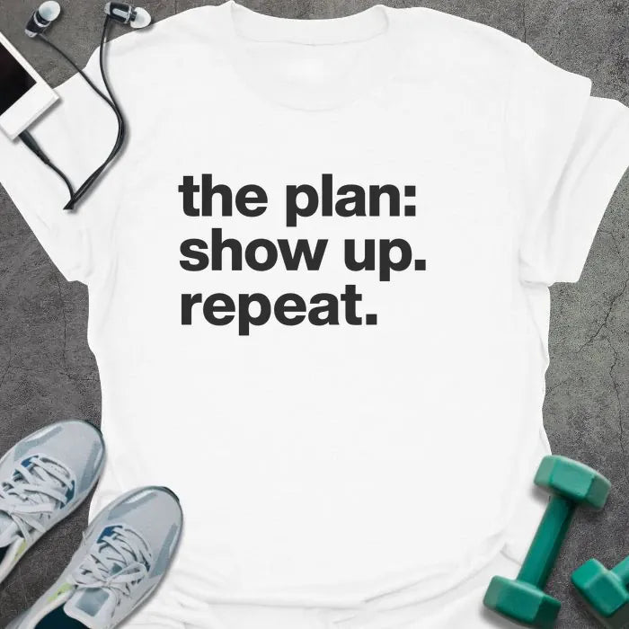 White t-shirt printed with "the plan: show up. repeat." in black lettering