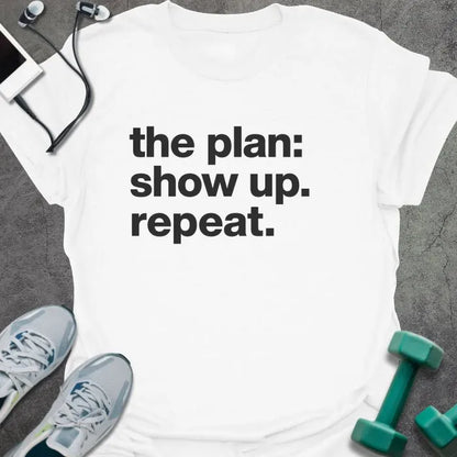 White t-shirt printed with "the plan: show up. repeat." in black lettering