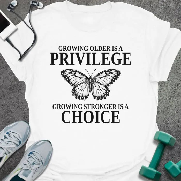 White t-shirt printed with "GROWING OLDER IS A PRIVILEGE, GROWING STRONGER IS A CHOICE" in black, with a line-drawn butterfly
