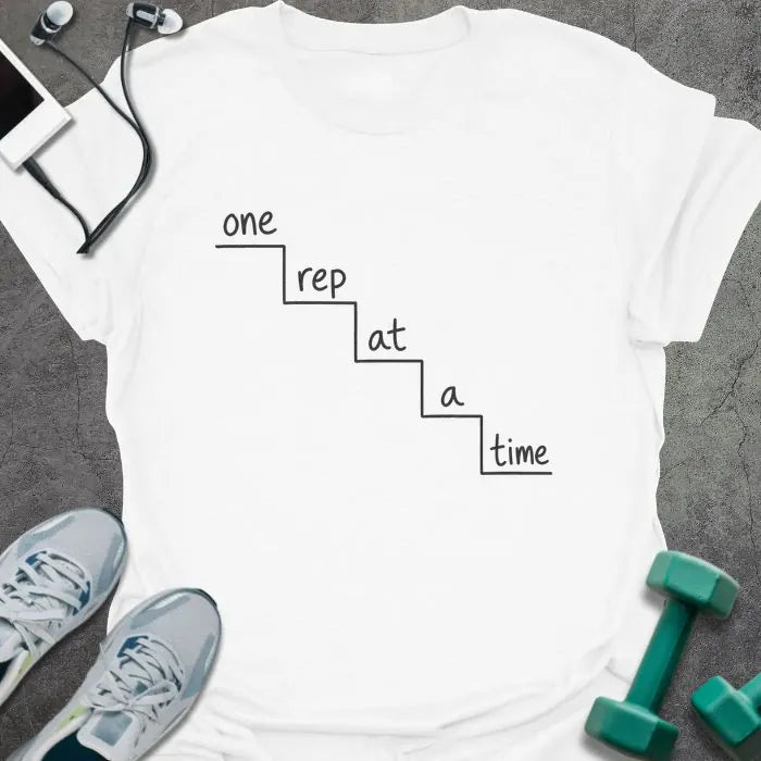 White t-shirt printed with "one rep at a time" in black line art, with staircase graphic