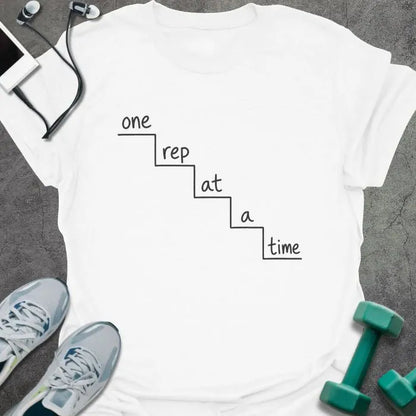 White t-shirt printed with "one rep at a time" in black line art, with staircase graphic