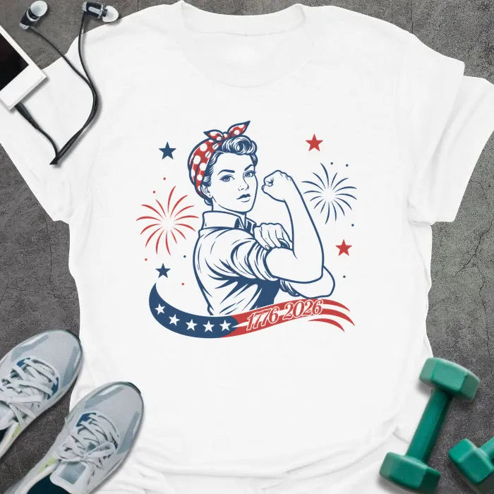 White t-shirt printed with "1776-2026" in navy, red, with Rosie the Riveter flexing her bicep among fireworks and stars