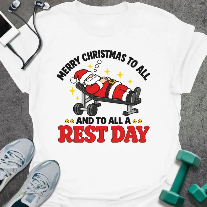 White t-shirt printed with "MERRY CHRISTMAS TO ALL AND TO ALL A REST DAY" in black and red, with Santa asleep on a weight bench