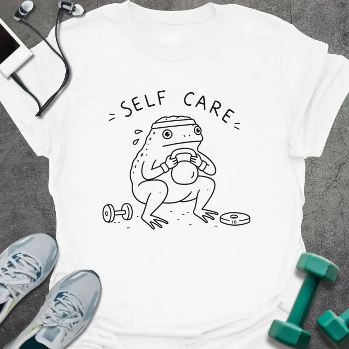 White t-shirt printed with "= SELF CARE =" in black, with figure exercising with kettlebell and dumbbells