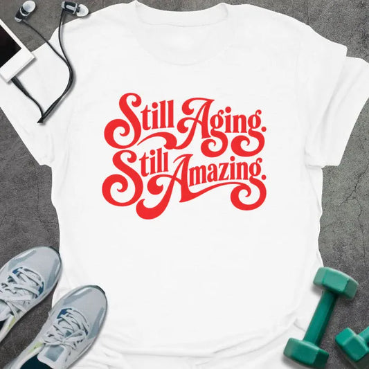 White t-shirt printed with "Still Aging. Still Amazing." in red decorative script lettering