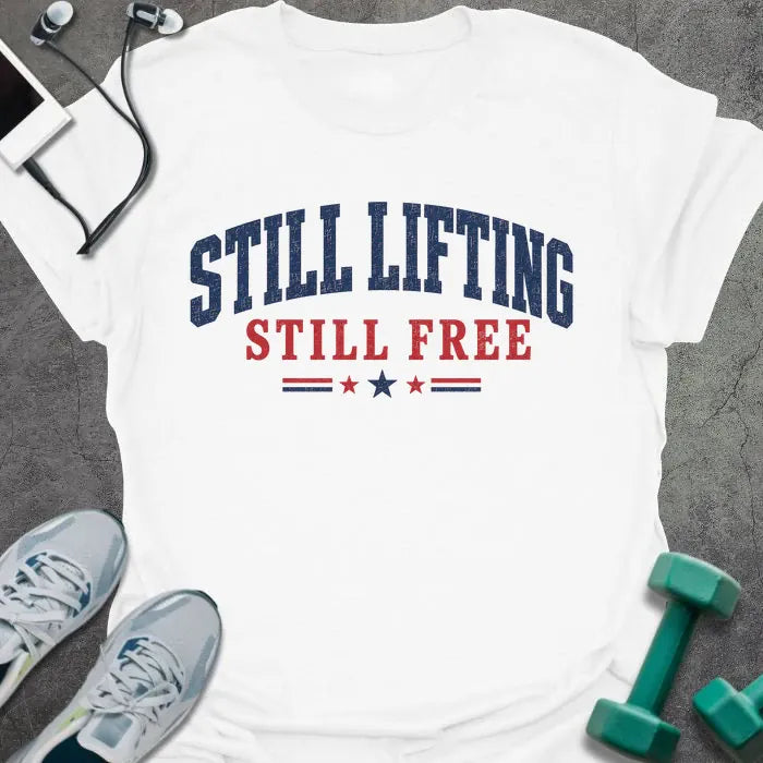 White t-shirt printed with "Still Lifting Still Free" in blue and red, with stars
