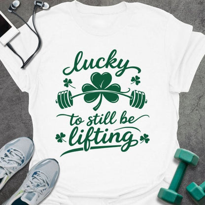 White t-shirt printed with "lucky to still be lifting" in green, with clover, shamrock and barbell