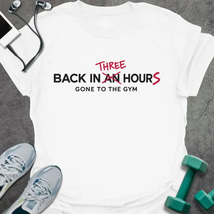 White t-shirt printed with "BACK IN AN HOUR, GONE TO THE GYM" in black, with "AN" crossed out and "THREE" and an extra S added in red to read back in three hours