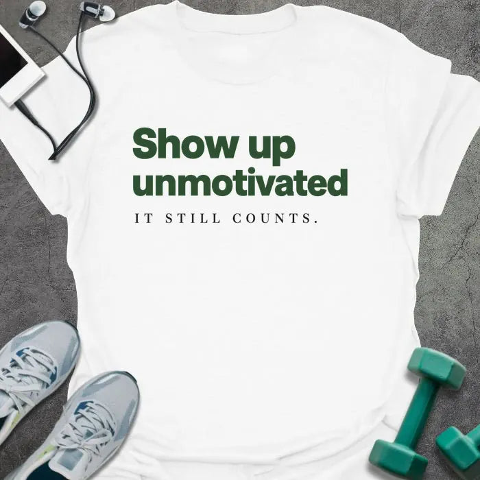 White t-shirt printed with "Show up unmotivated IT STILL COUNTS." in green and black