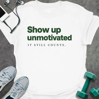 White t-shirt printed with "Show up unmotivated IT STILL COUNTS." in green and black