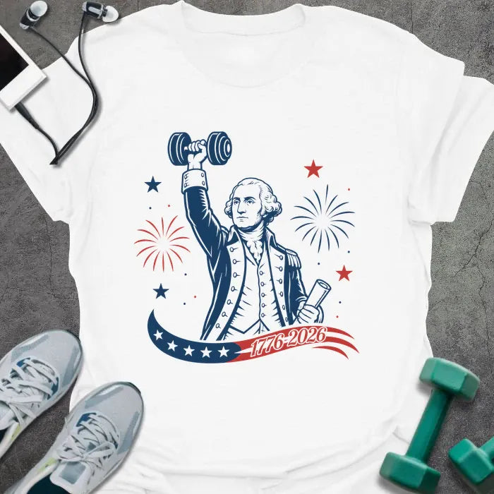 White t-shirt printed with "1776-2026" in navy, red, with George Washington holding a dumbbell overhead and a scroll, fireworks and stars