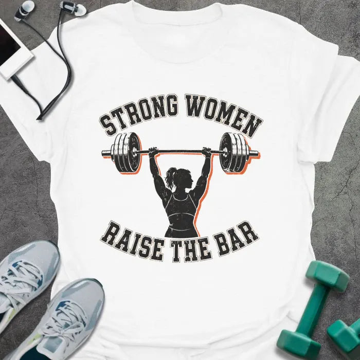 White t-shirt printed with "STRONG WOMEN RAISE THE BAR" in black lettering, with a silhouette of a woman weightlifter raising a barbell overhead