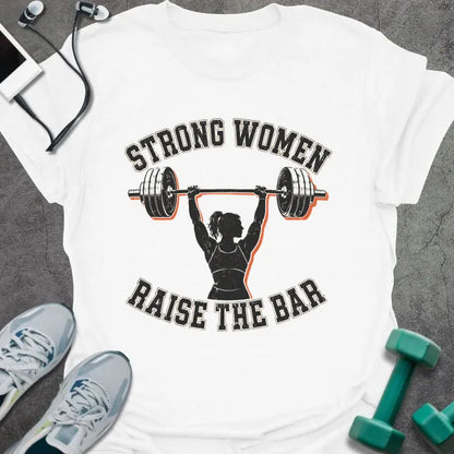 White t-shirt printed with "STRONG WOMEN RAISE THE BAR" in black lettering, with a silhouette of a woman weightlifter raising a barbell overhead
