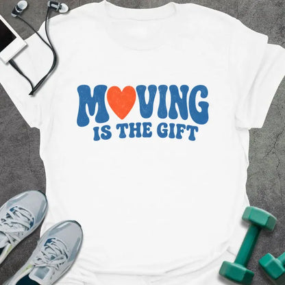 White t-shirt printed with "MOVING IS THE GIFT" in blue and orange text with a heart replacing the O