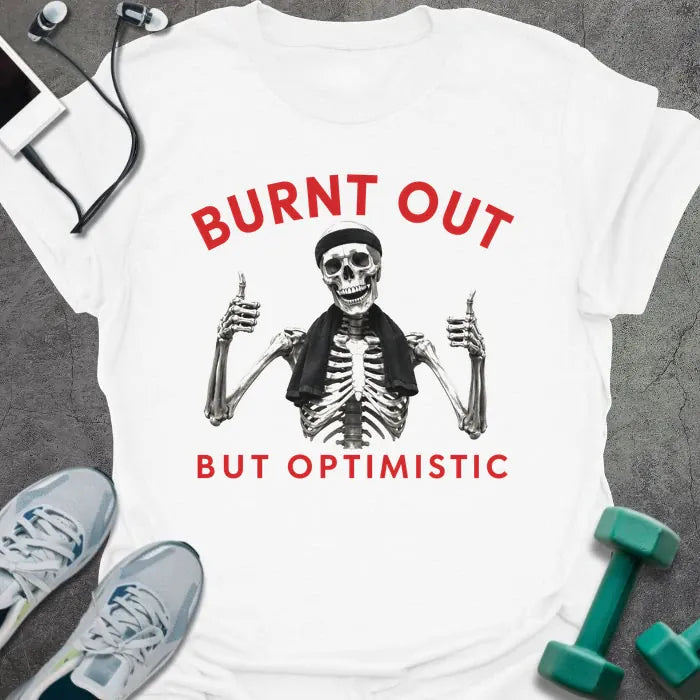 White t-shirt printed with "BURNT OUT but OPTIMISTIC" in red and black, with skeleton with dumbbells