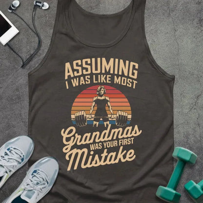 Dark grey tank top printed with "ASSUMING I WAS LIKE MOST Grandmas WAS YOUR FIRST MISTAKE" in tan and orange, with silhouette and sunset stripes