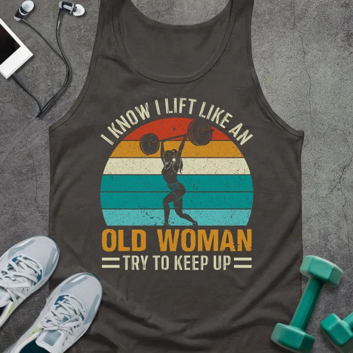 Dark grey tank top printed with "I Know I Lift Like an Old Woman Try to Keep Up" in white, orange, and teal, with silhouette and sunset stripes