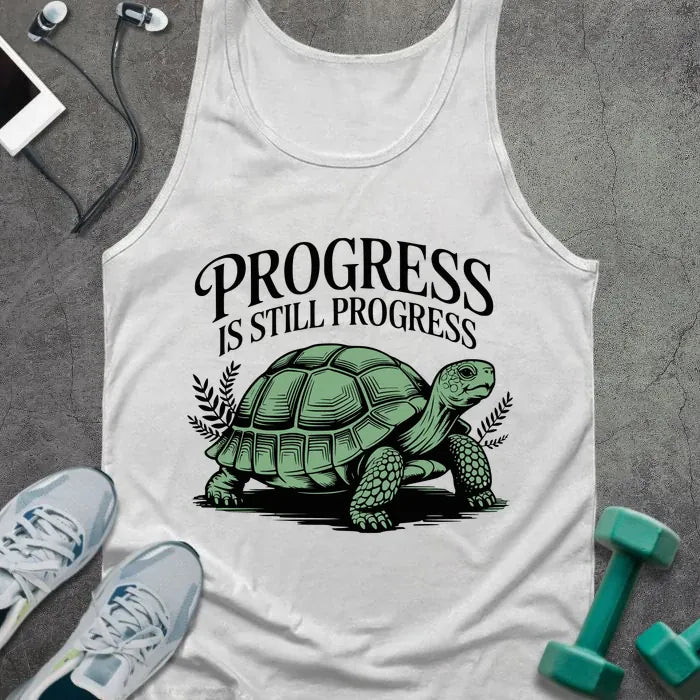 White tank top printed with "Progress is Still Progress" in black and green, with a turtle graphic